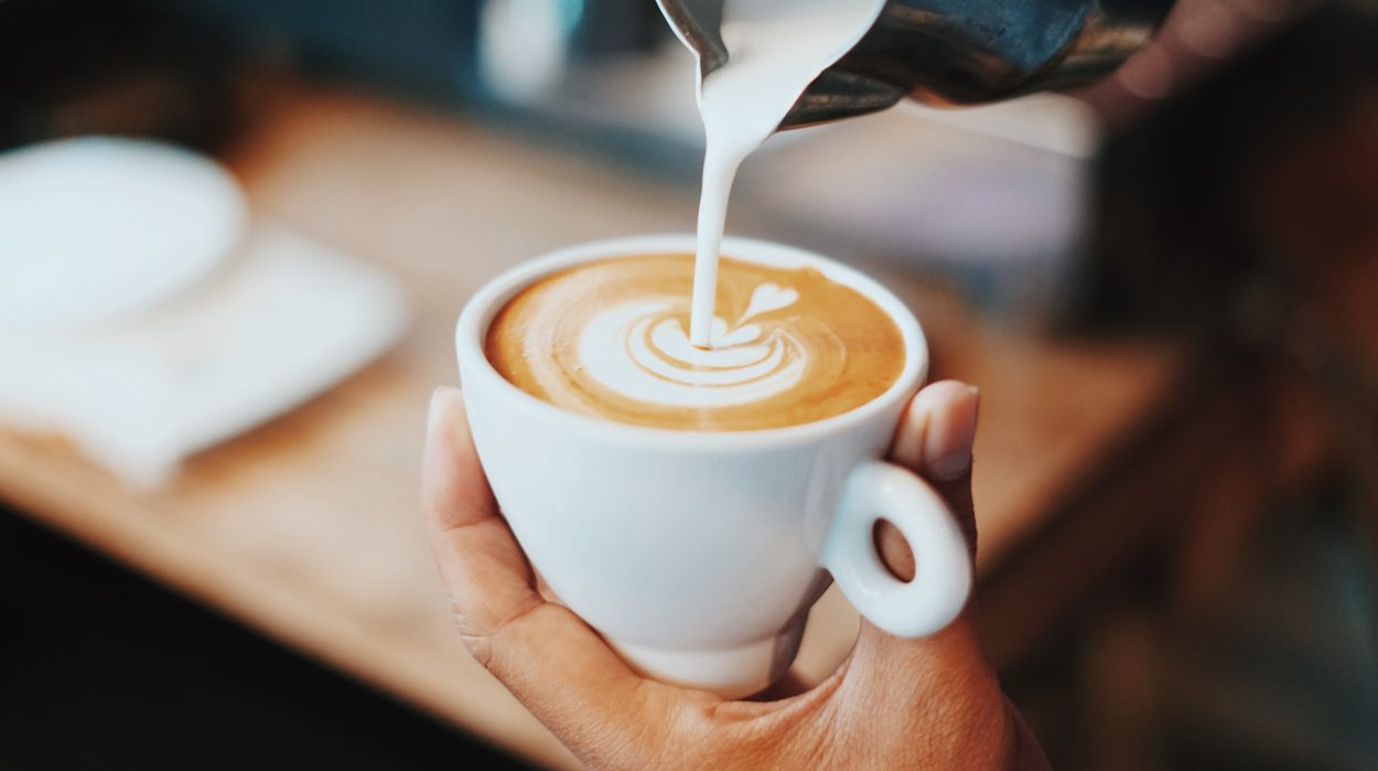 milk being poured into a small cup of coffee