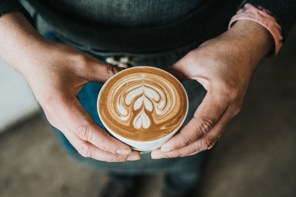 A beautiful cup of latte with foam art being held by a barista.