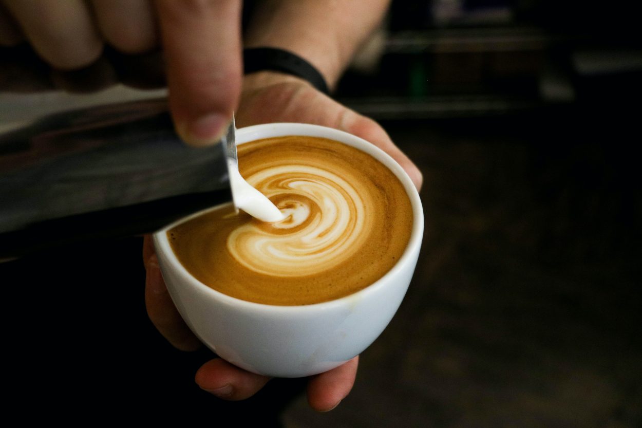 A picture showing a hand of barista properly showing how to pour milk into an espresso shot.
