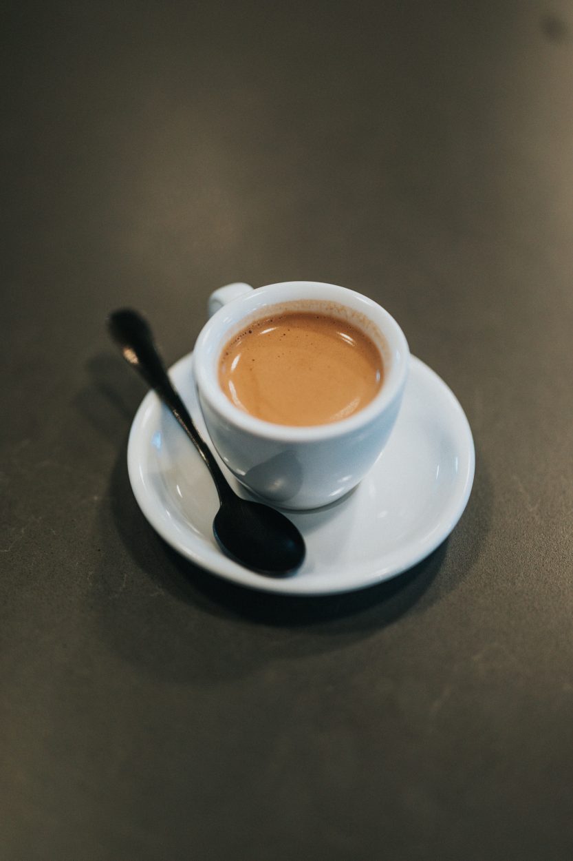 An espresso shot in a white shot mug on a white saucer.