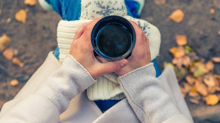 A girl in white sweater holding a cup of coffee.