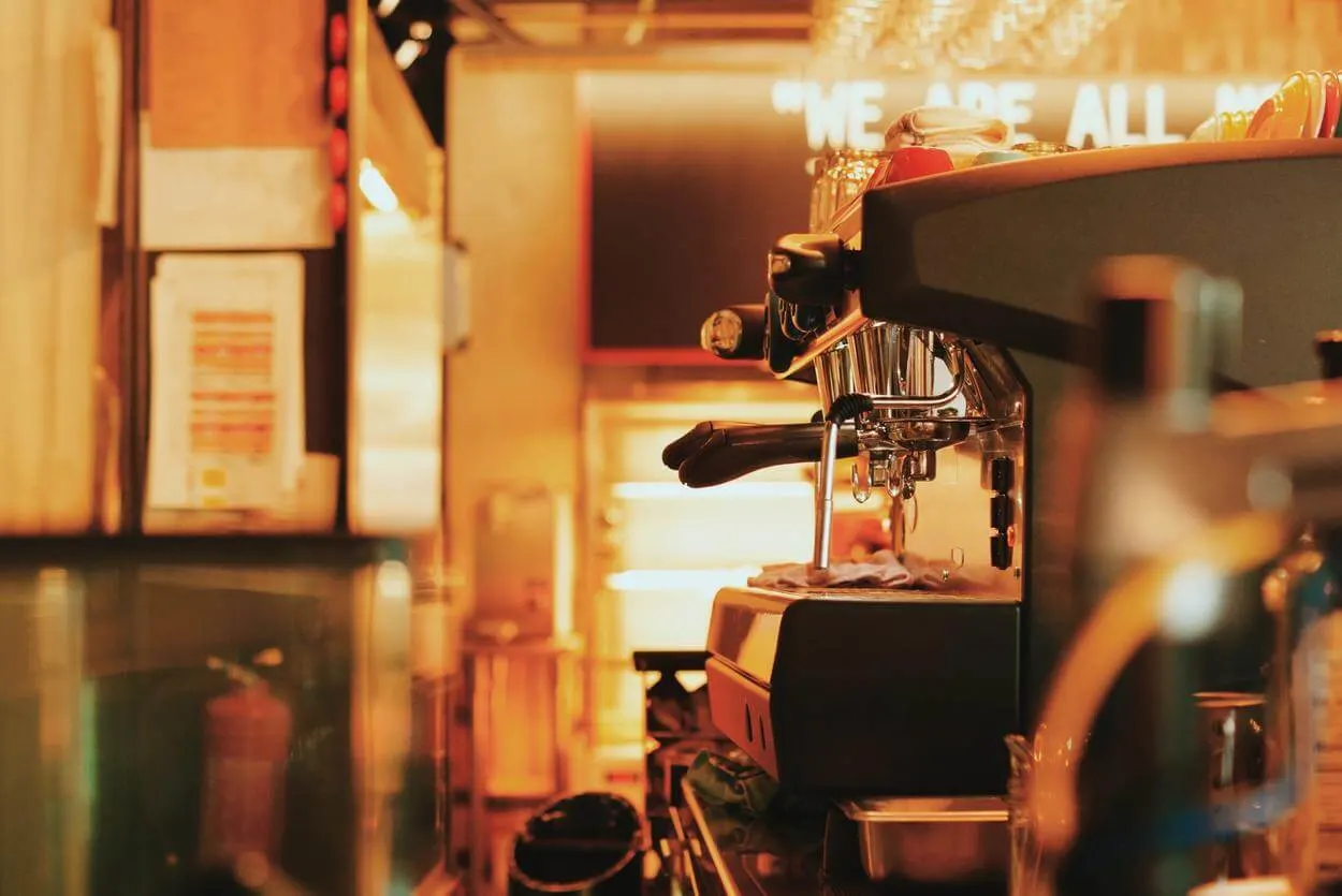 A side view of a coffee machine in a coffee shop in sepia lighting.