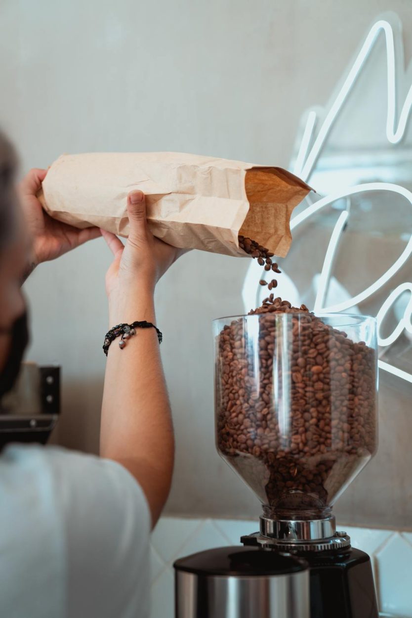 A barista putting coffee grounds in a big electric grinder.