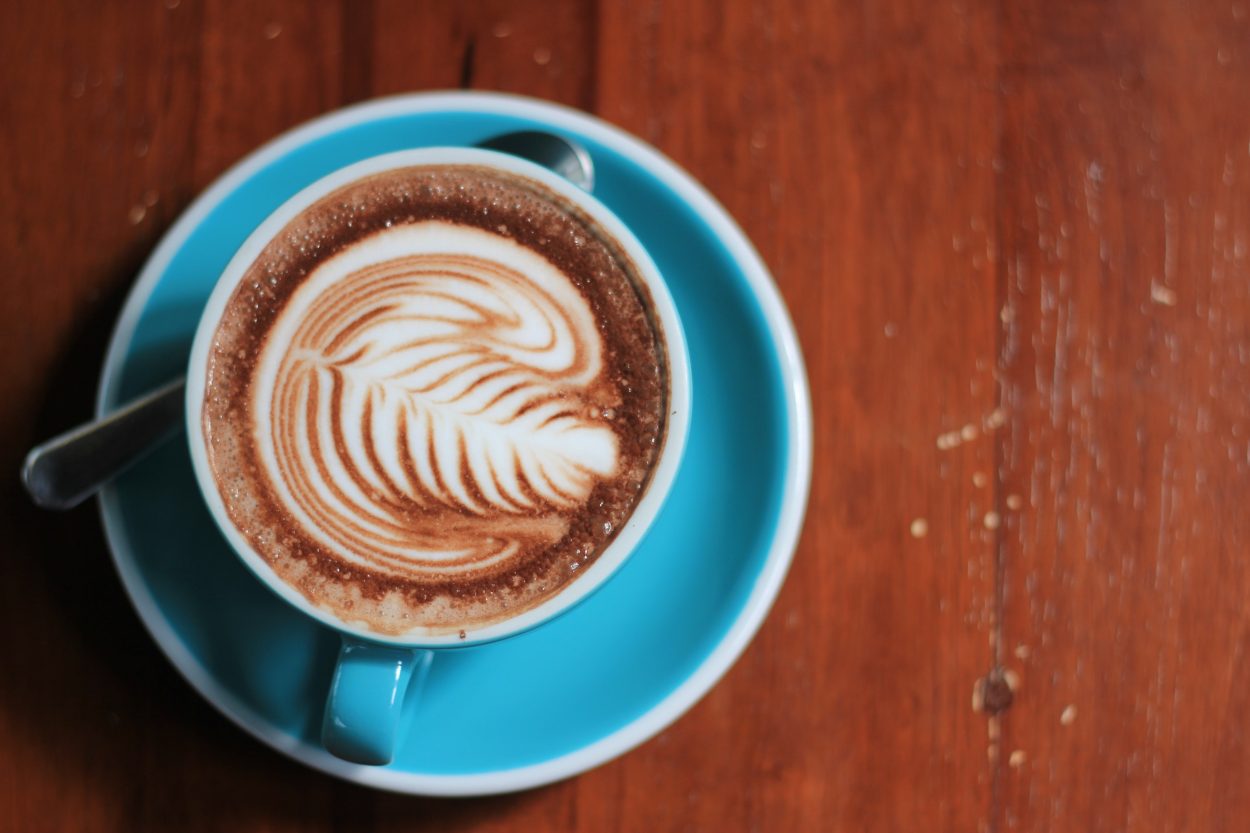 Top view of a latte in a light blue cup and saucer showing latte art in a leaf design.