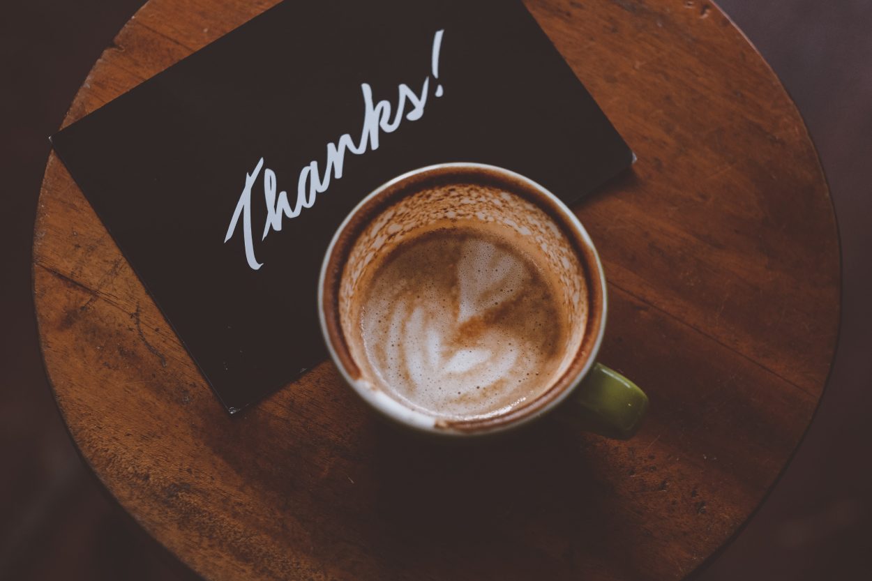 a cup of coffee next to a card that says thank you
