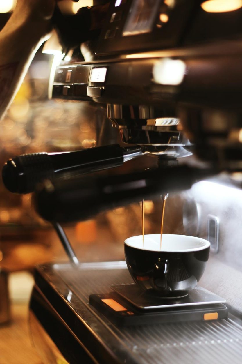 Freshly brewed espresso dripping on a black cup.