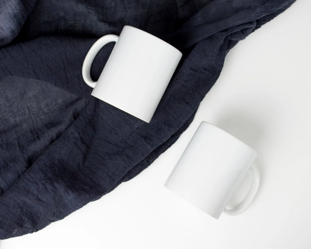 two white mugs, one on a dark blanket