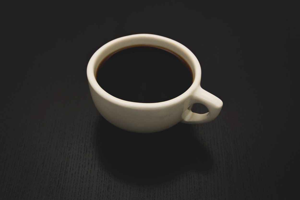Black coffee in a white cup on top a dark colored tabletop.
