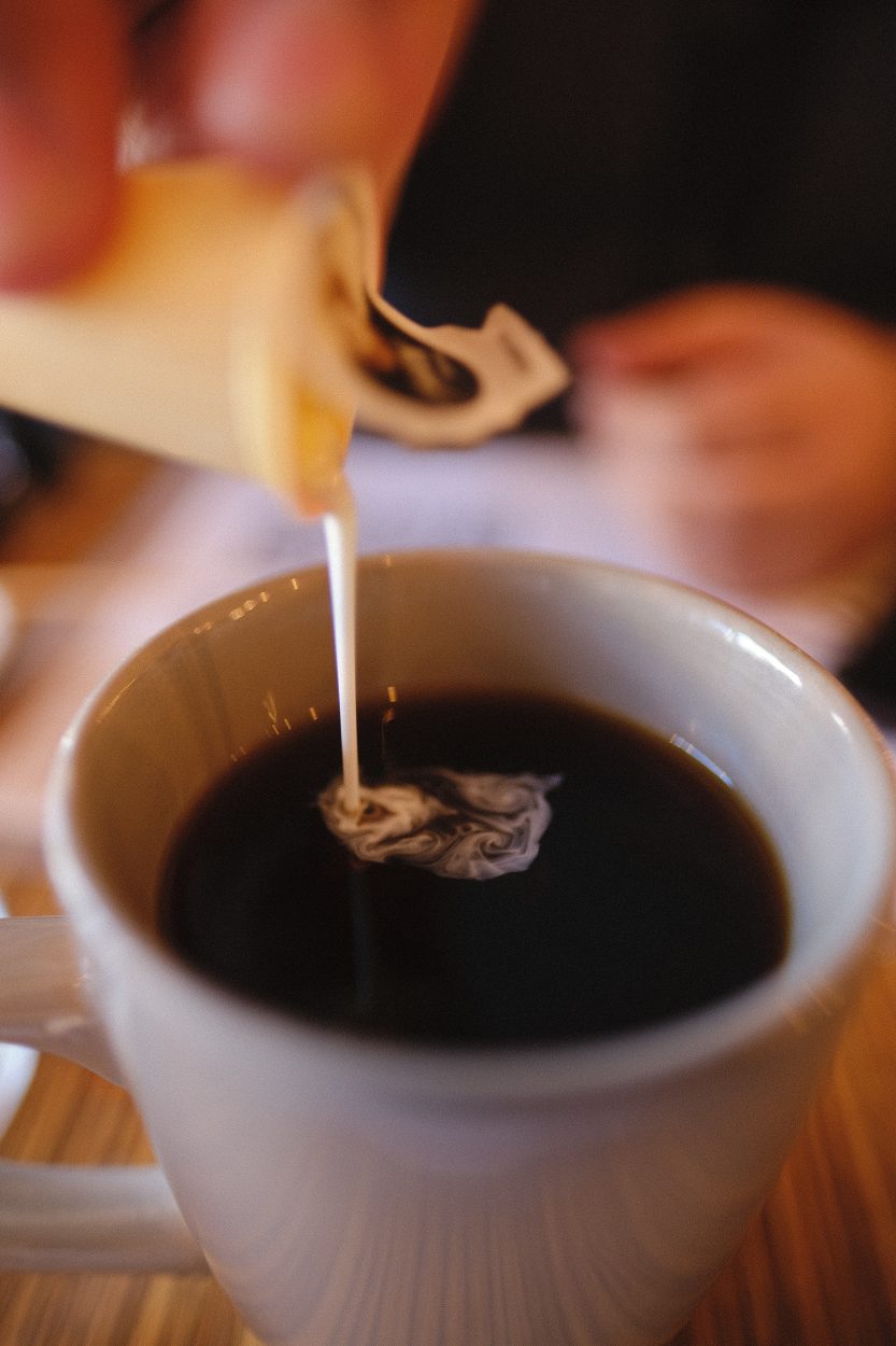 pouring cream into black coffee
