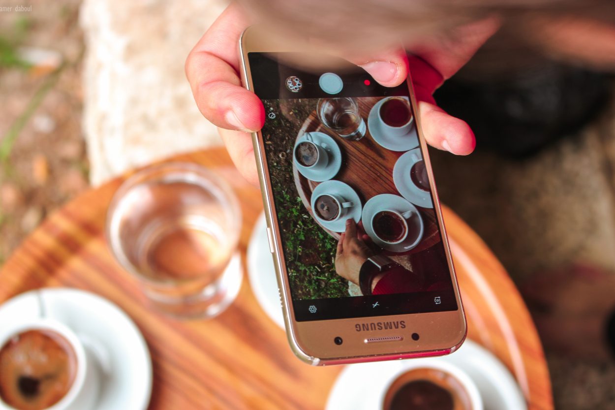 A Samsung phone being used to capture a picture of different kinds of coffee in white cups.
