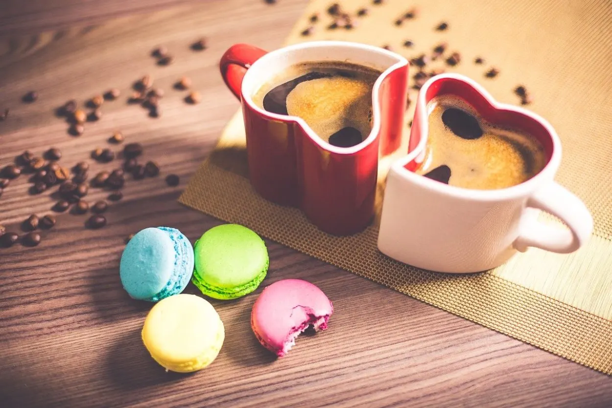 two heart shaped mugs next to each other with different colored macaroons