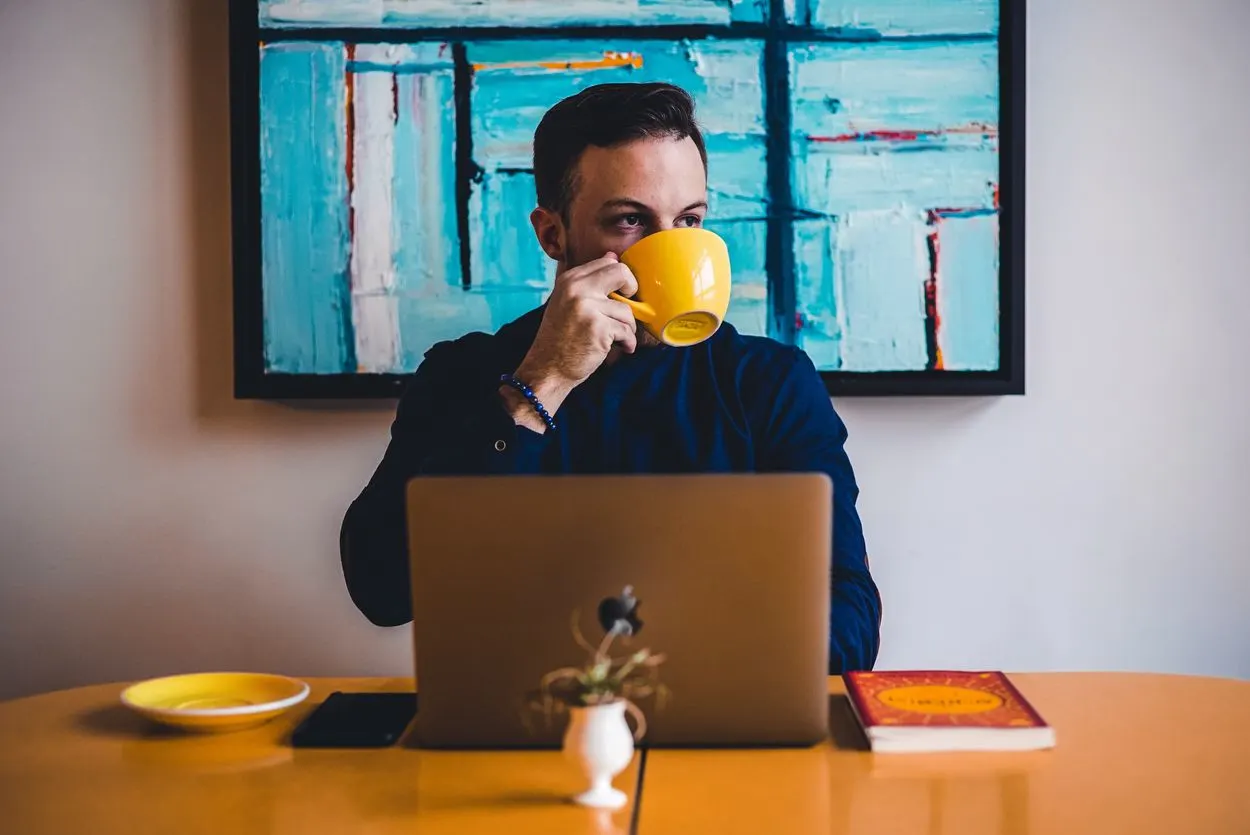 a person on their laptop drinking coffee from a yellow cup