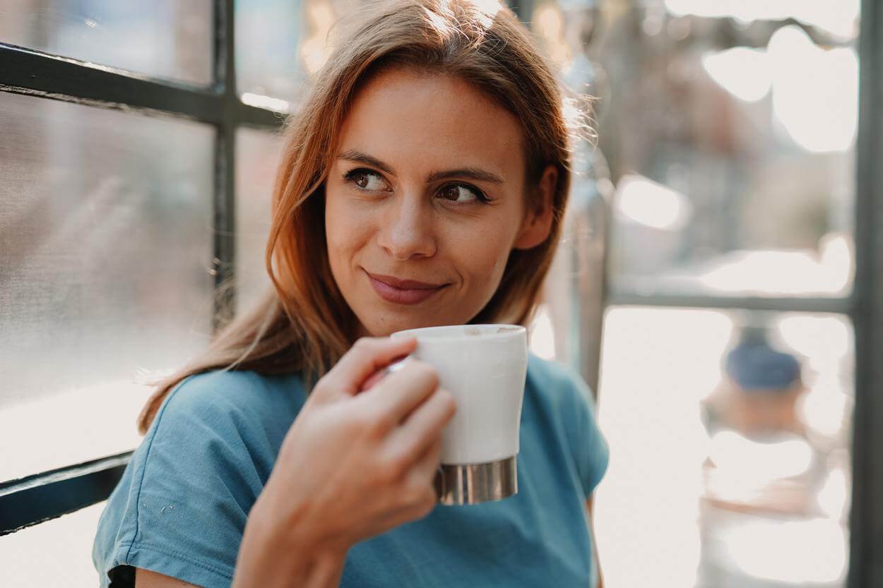 A woman smiling and holding a white cup.