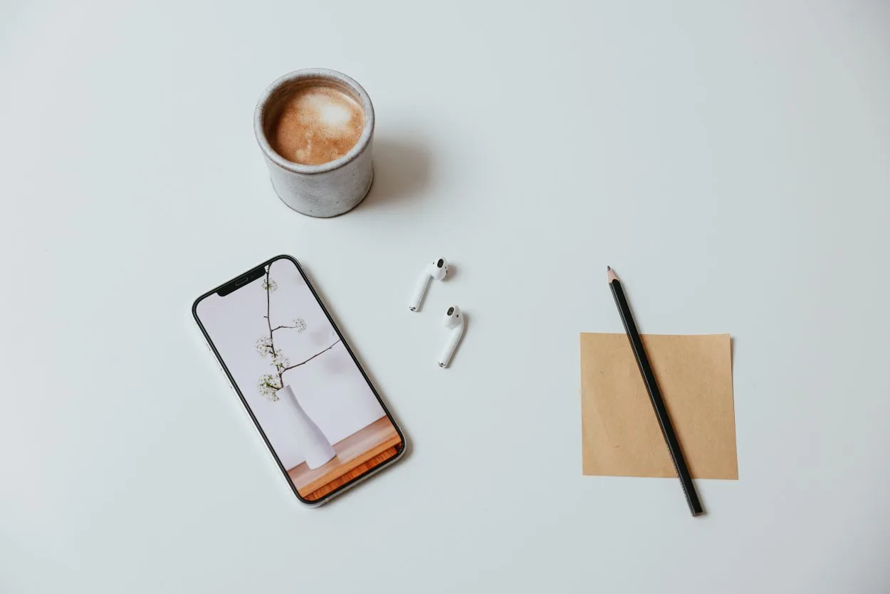 Top view showing a mobile phone, earbuds, a cup of coffee and a notepad with a pencil.