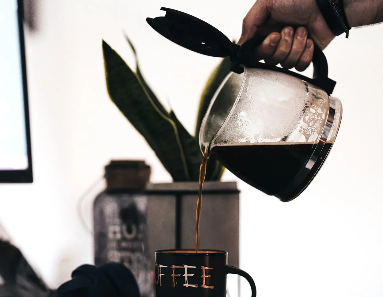 someone pouring a freshly brewing coffee from the pot into a mug