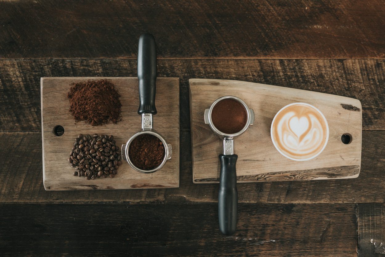 two wooden tray filled with roasted coffee beans, ground of coffee, cup of latte 