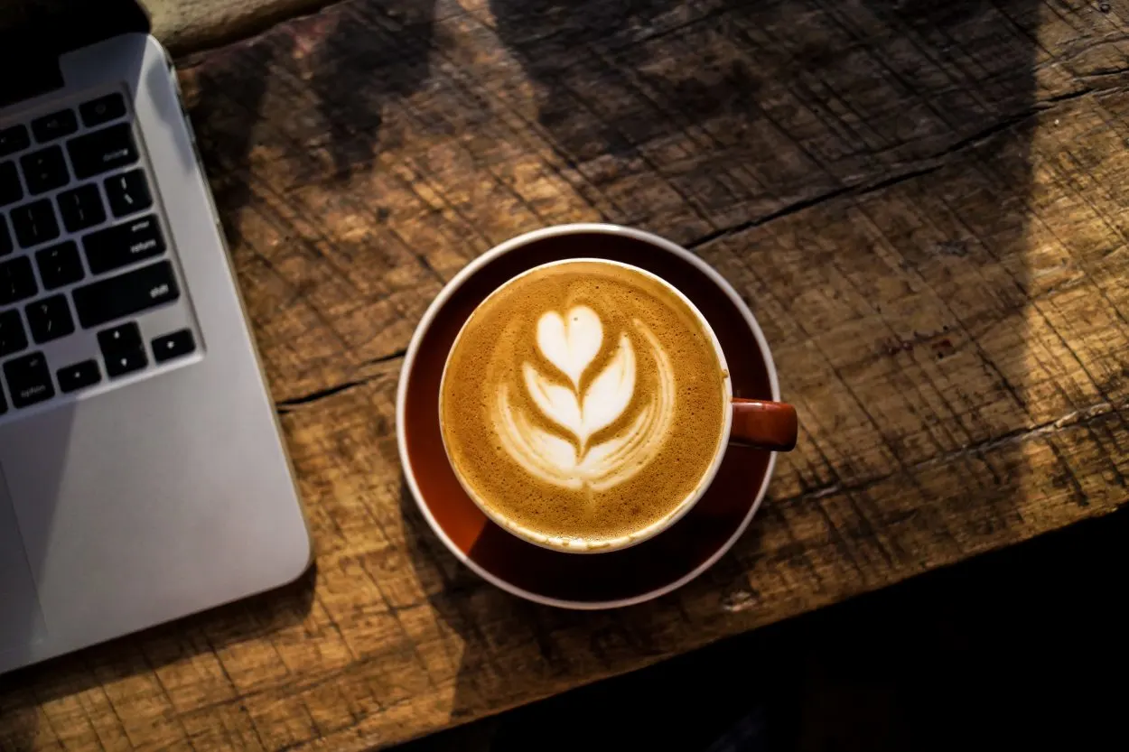 a cup of coffee on a wooden desk next to a laptop