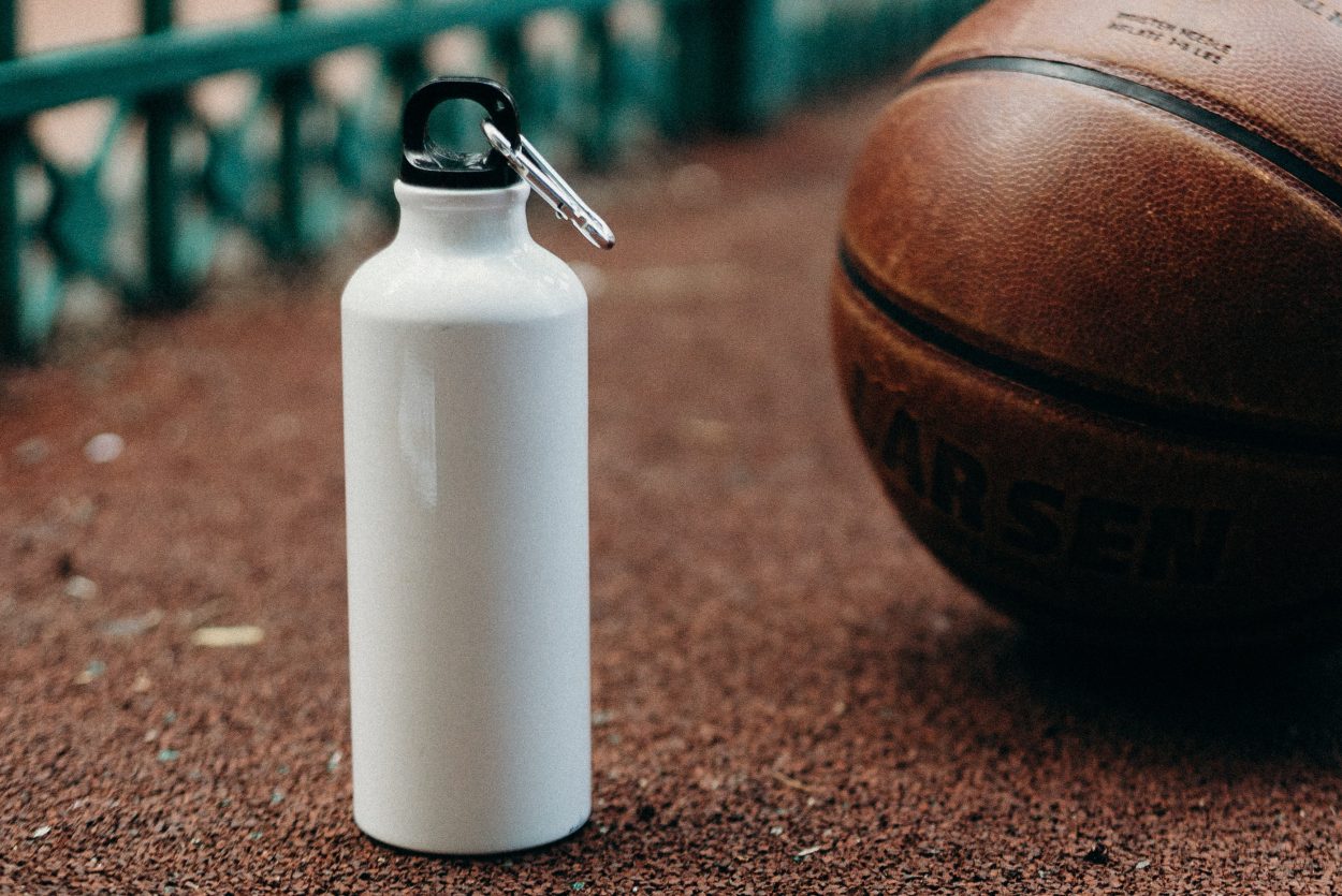 A white insulated container taken outdoors beside a basketball.