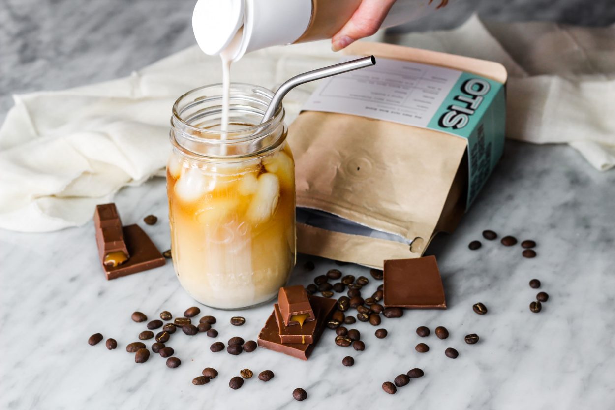 Cold brew coffee with ice and milk with coffee beans and chocolate on its sides.