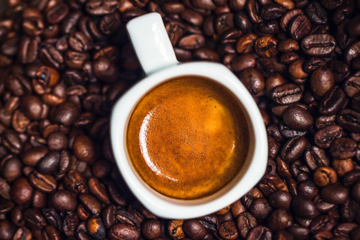 A top shot of espresso in a white cup with coffee beans underneath.