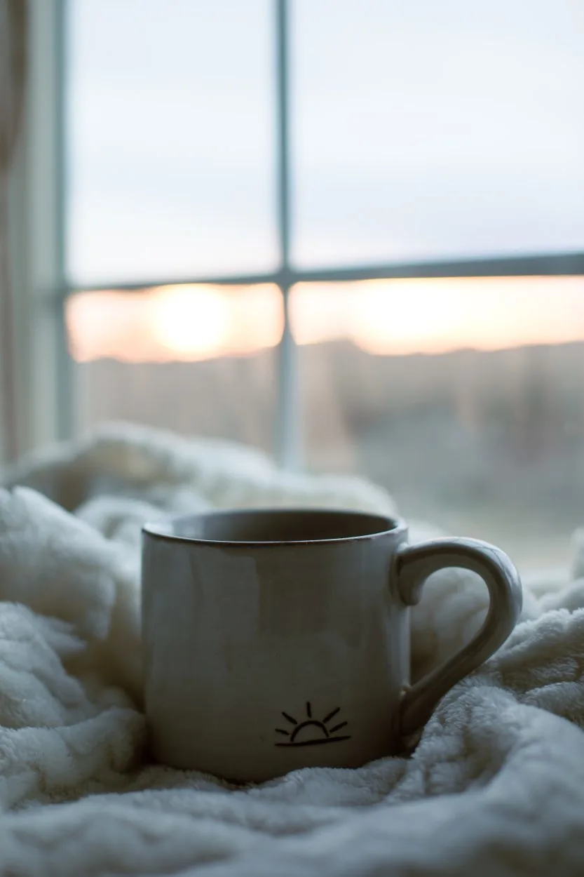 A coffee mug with a simple rising sun design atop a flannel  cloth.