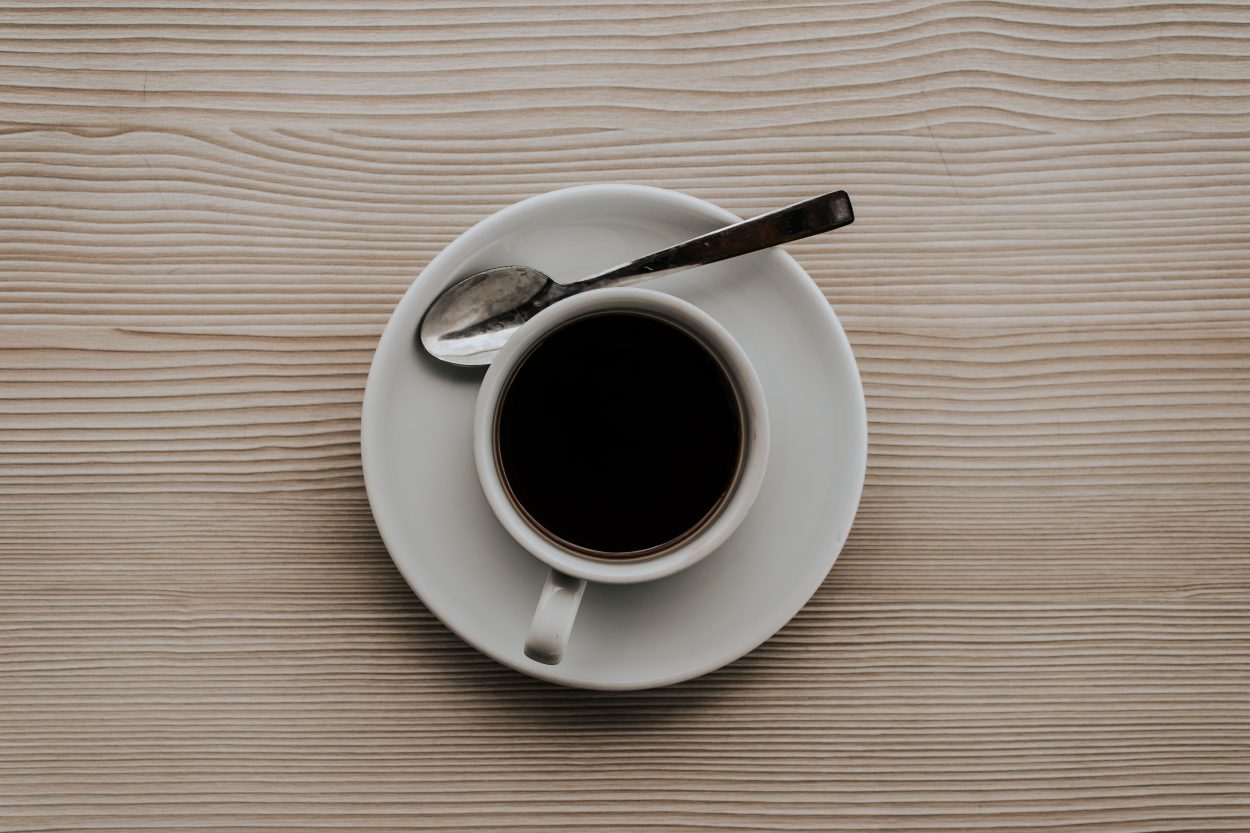 A white mug containing black coffee on a wooden table.