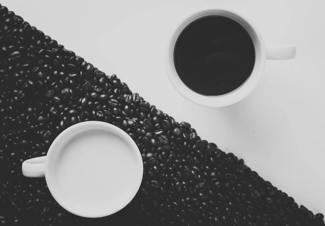 Two ceramic mugs containing black coffee and milk.