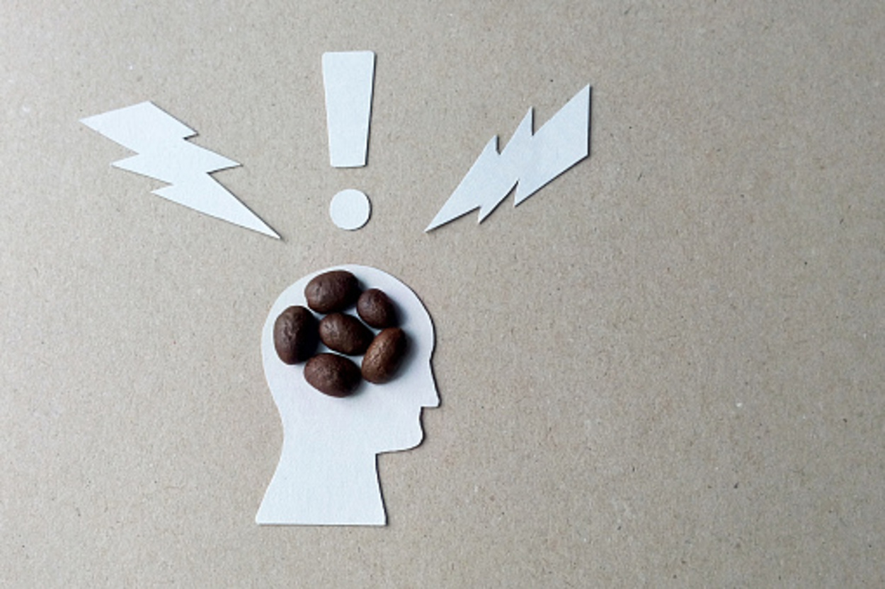 Five coffee beans are placed on a white cardboard cut in the shape of a human head.