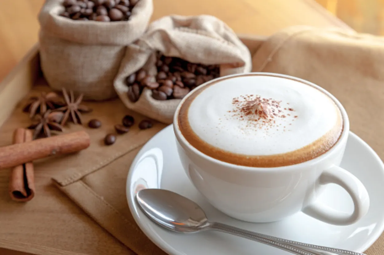 A cup of cappuccino with a bag of coffee beans