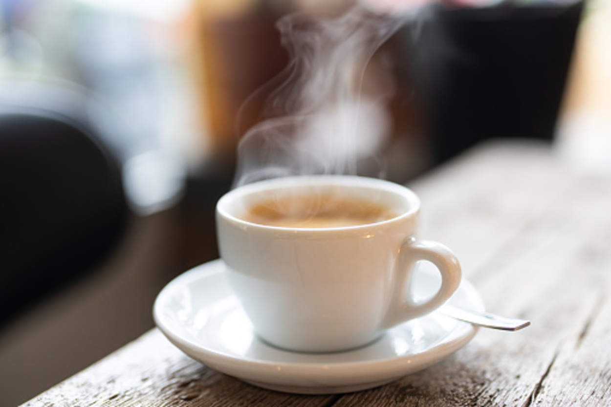 Steam rising from a white cup of latte with a spoon on a saucer over a wooden table in the