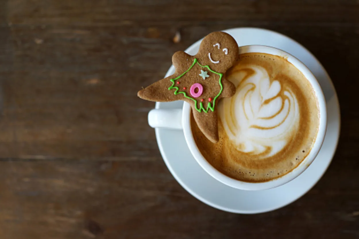 A cup of gingerbread latte on a wooden table with a gingerbread sitting on the top of cup