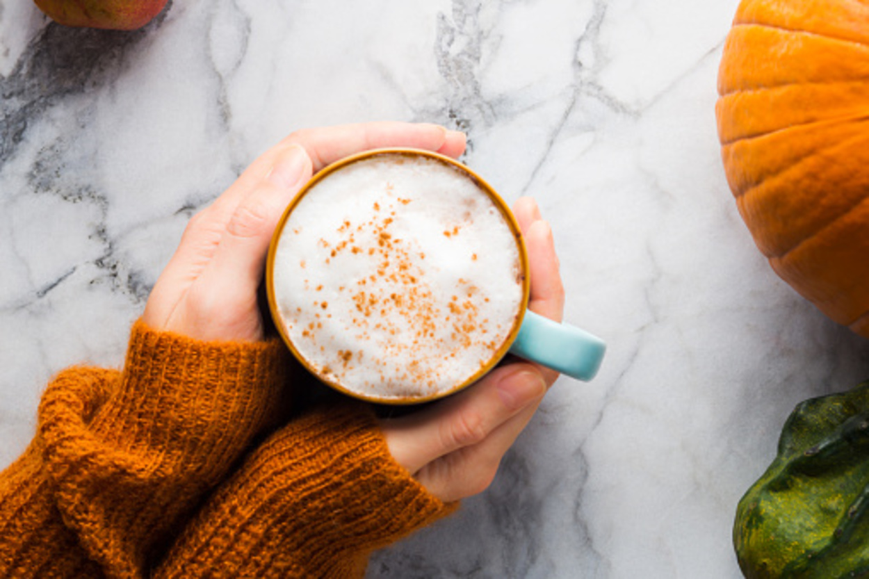A pumpkin spice latte cup in a woman's hand on a marble top