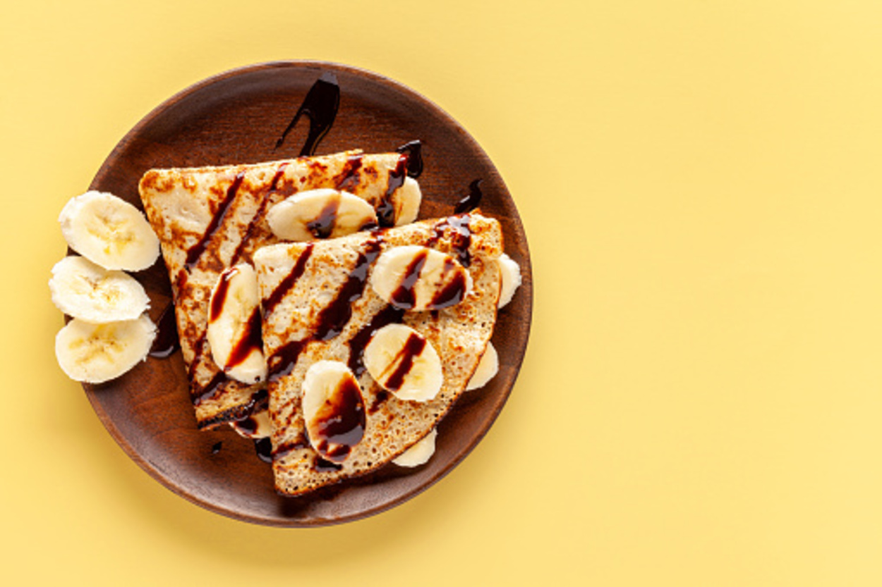 Crepes on a wooden plate on a yellow background. 