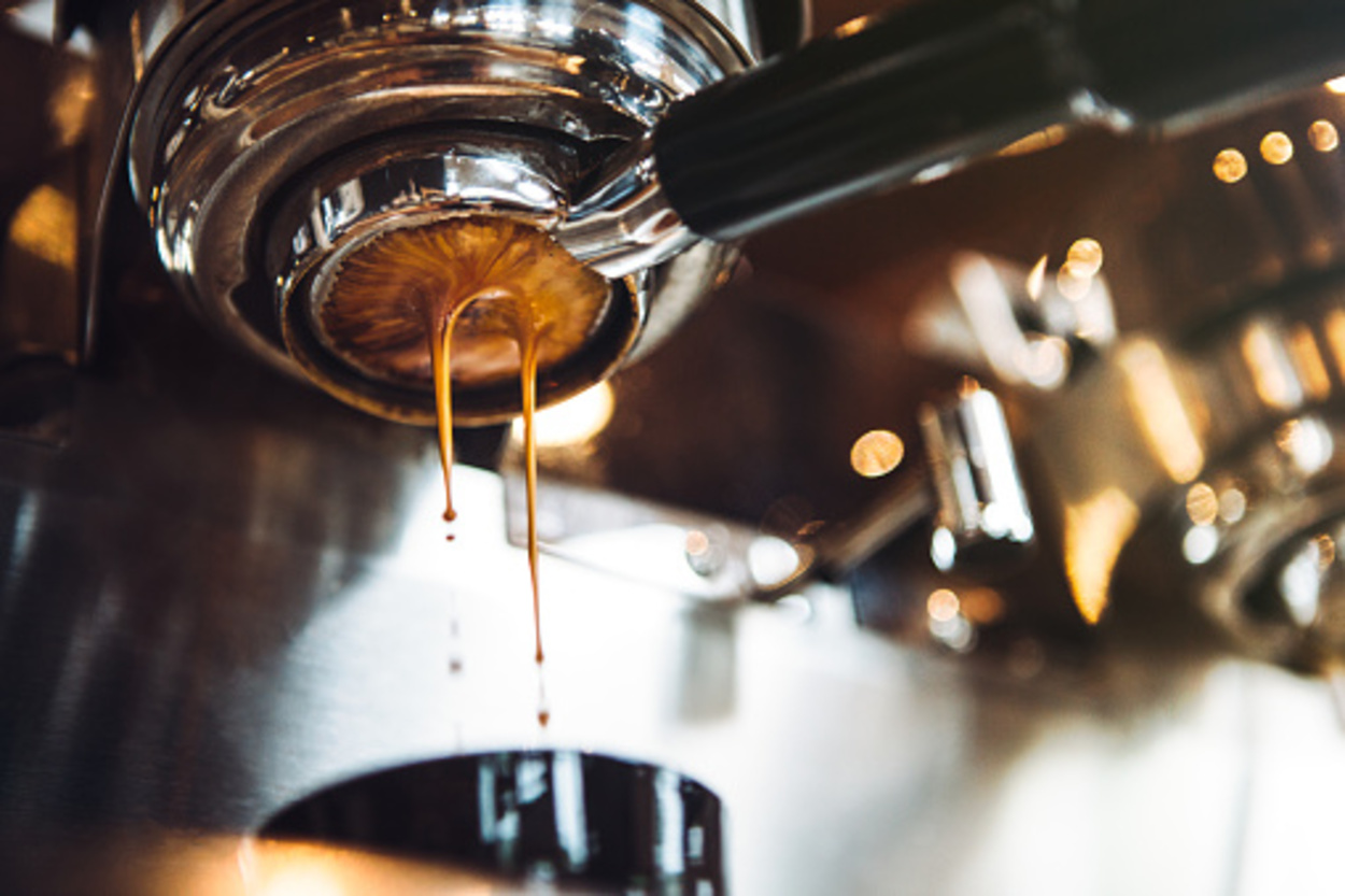 Fresh and hot espresso coffee pours from a portafilter on a nice chrome espresso machine