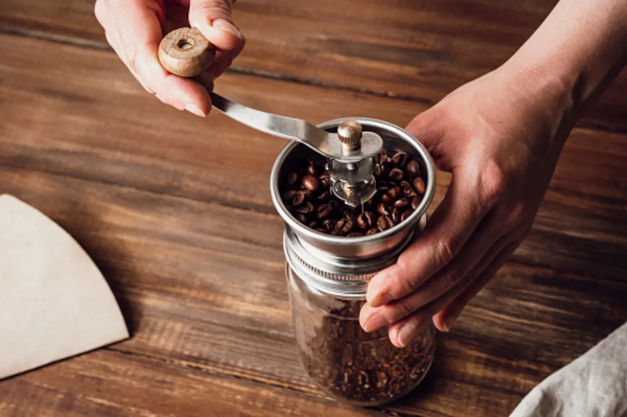 Grinding coffee beans in a manual coffee grinder on a wooden table.