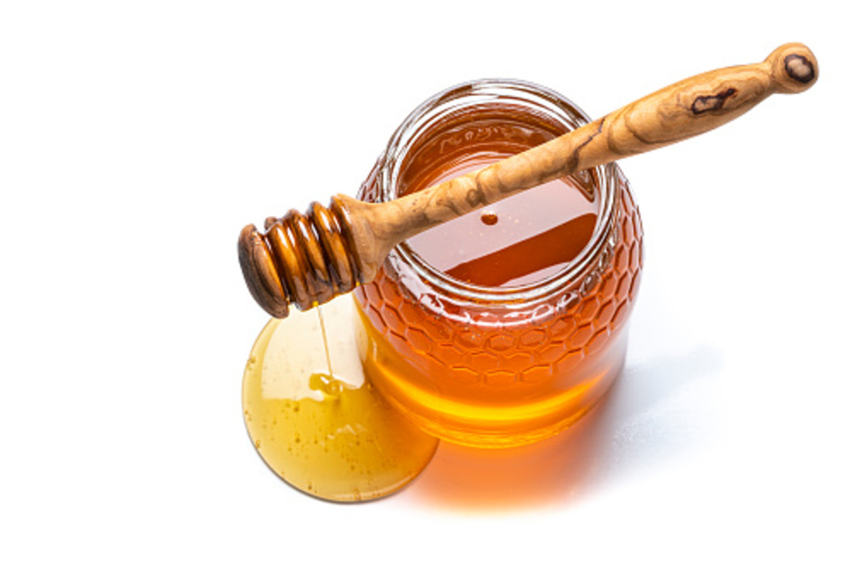 A jar of honey with a honey dipper dripping with honey placed upon it