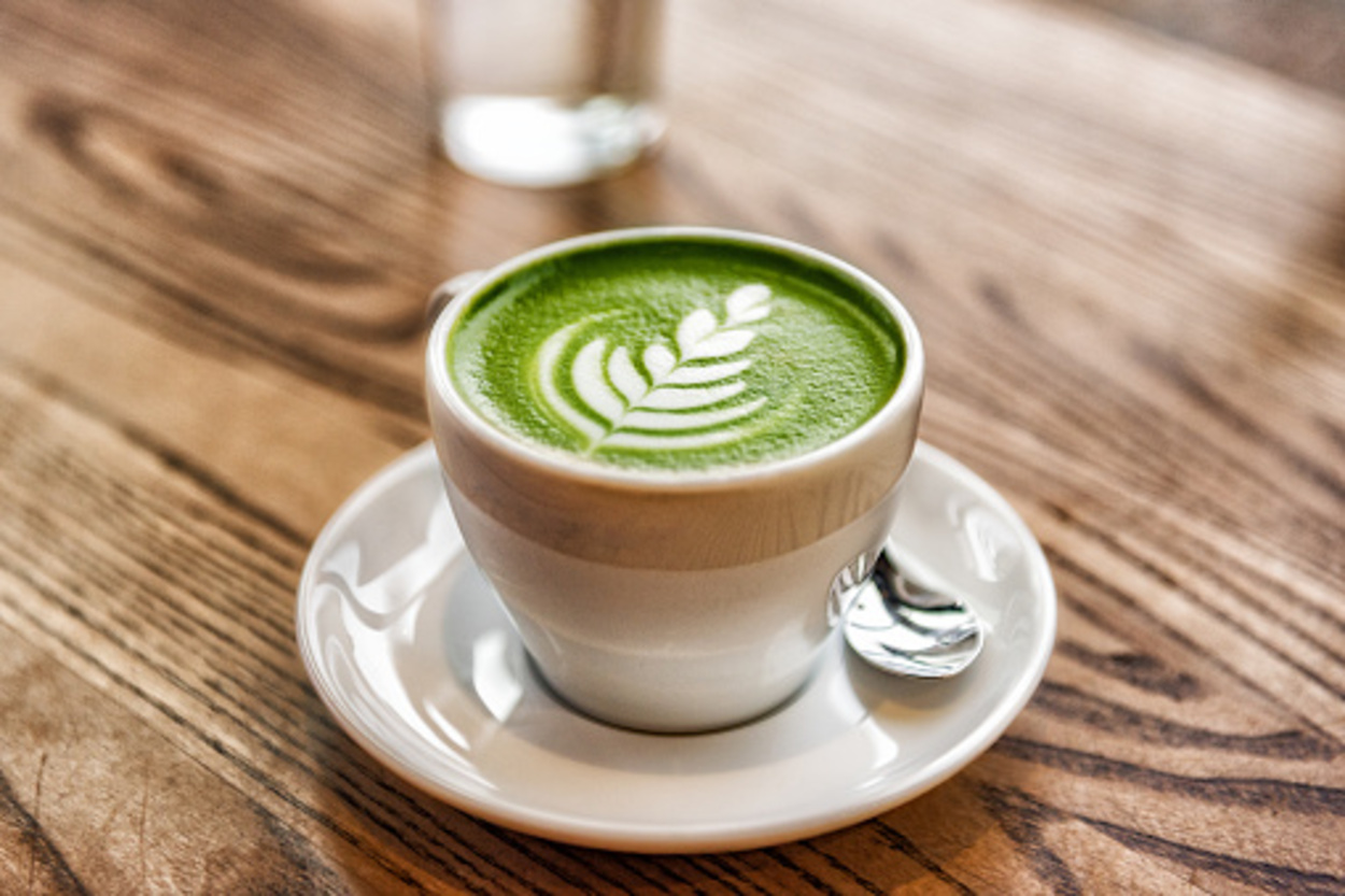 Matcha latte green milk foam cup on wood table at a café. 