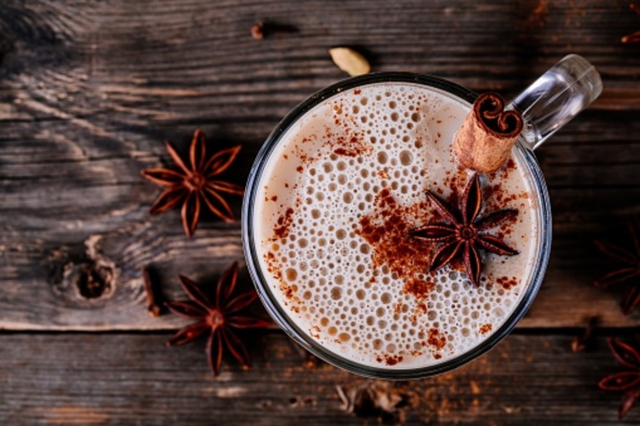 Homemade Chai Tea Latte with anise and cinnamon stick in glass mug on wooden rustic background. Top view