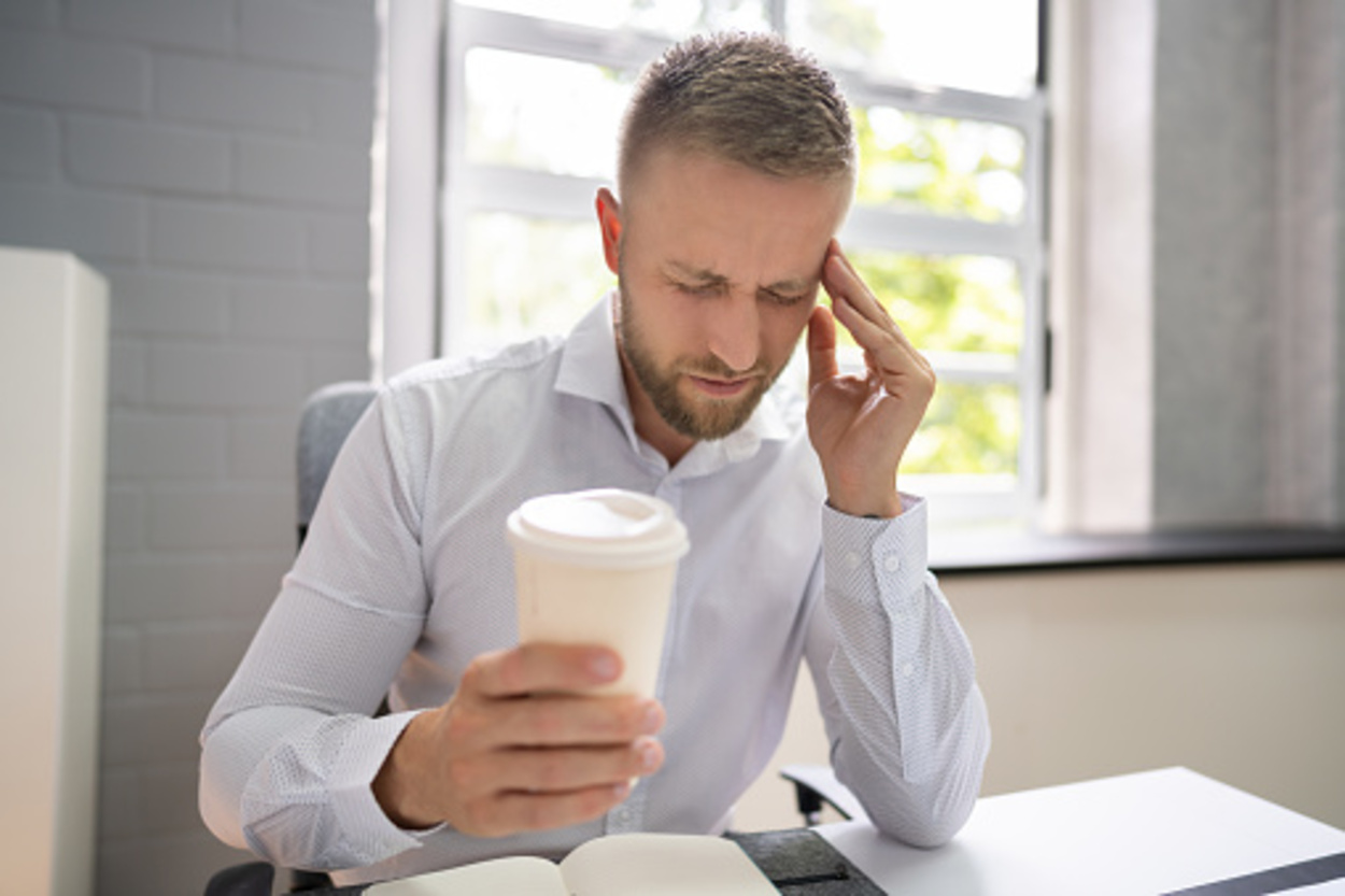 a person holding coffee in one hand and his head with the other hand depicting headache