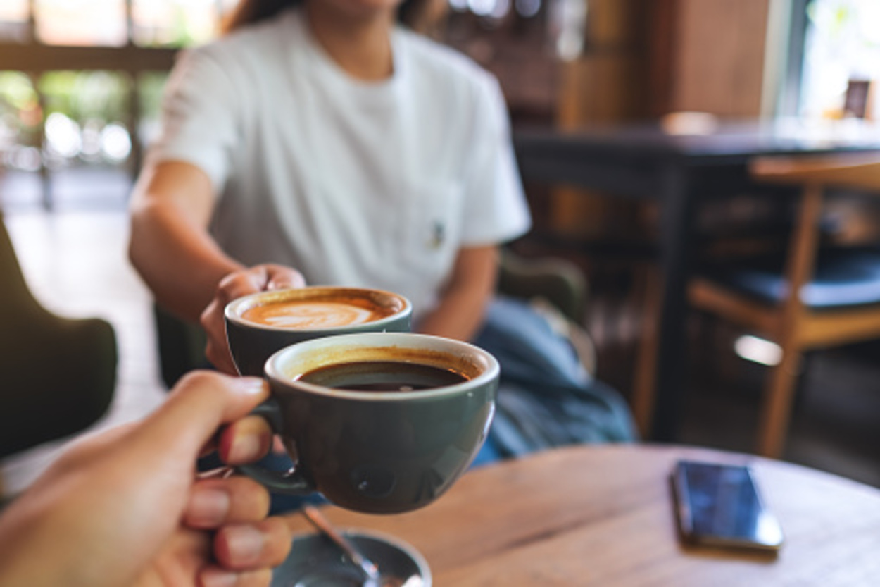Closeup image of a man and a woman clinking coffee mugs in a cafe