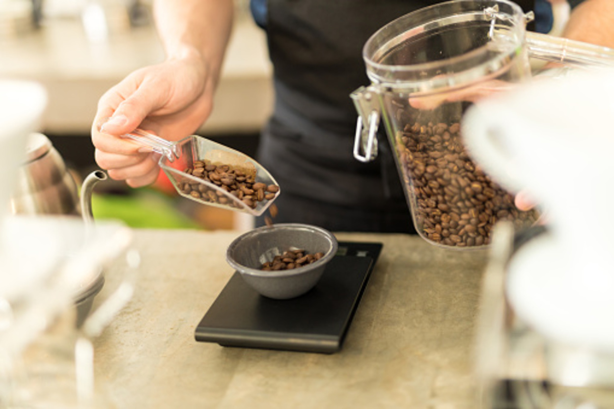 Closeup of a male barista pouring coffee grains on a scale before brewing some coffee in a cafe