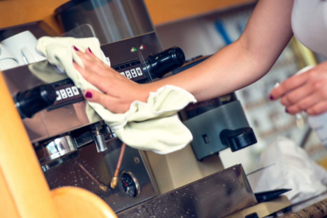 Waitress cleaning coffee machine with a cloth.