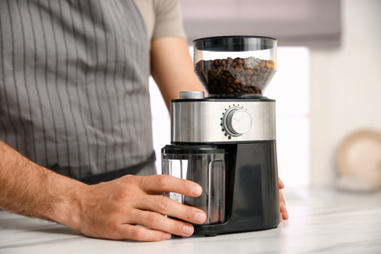 Man using an electric coffee grinder in kitchen, closeup