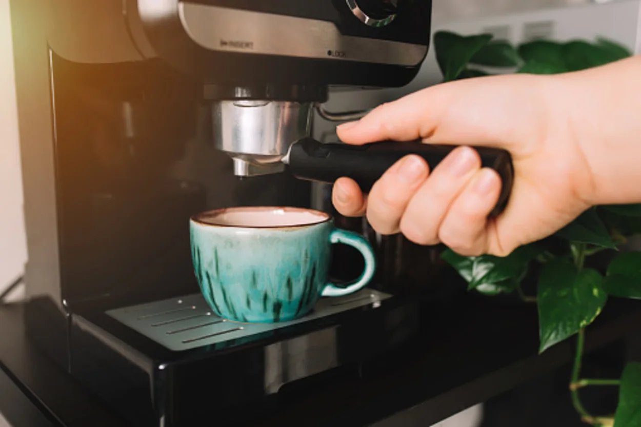Hand holding portafilter, a green cup of coffee at the coffee maker machine, coffee time. 